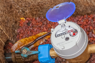 Compteur d'eau en fosse avec couvercle bleu ouvert, cadran de mesure en m³ visible et robinet de coupure bleu